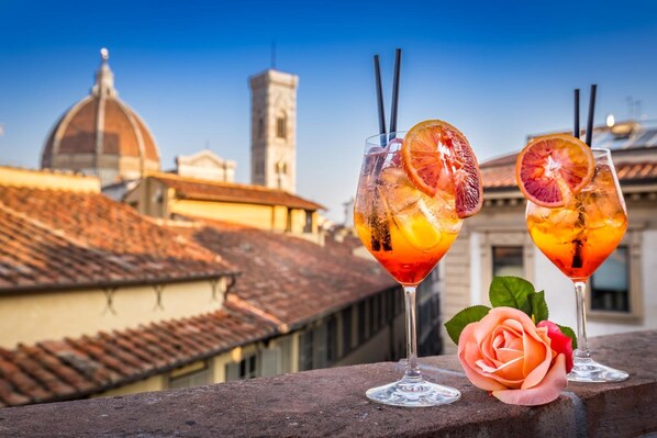 Two cocktails with fruit garnishes on a balcony with a cityscape in the background. - Palazzo dei Conti residenza d'Epoca (Florence)