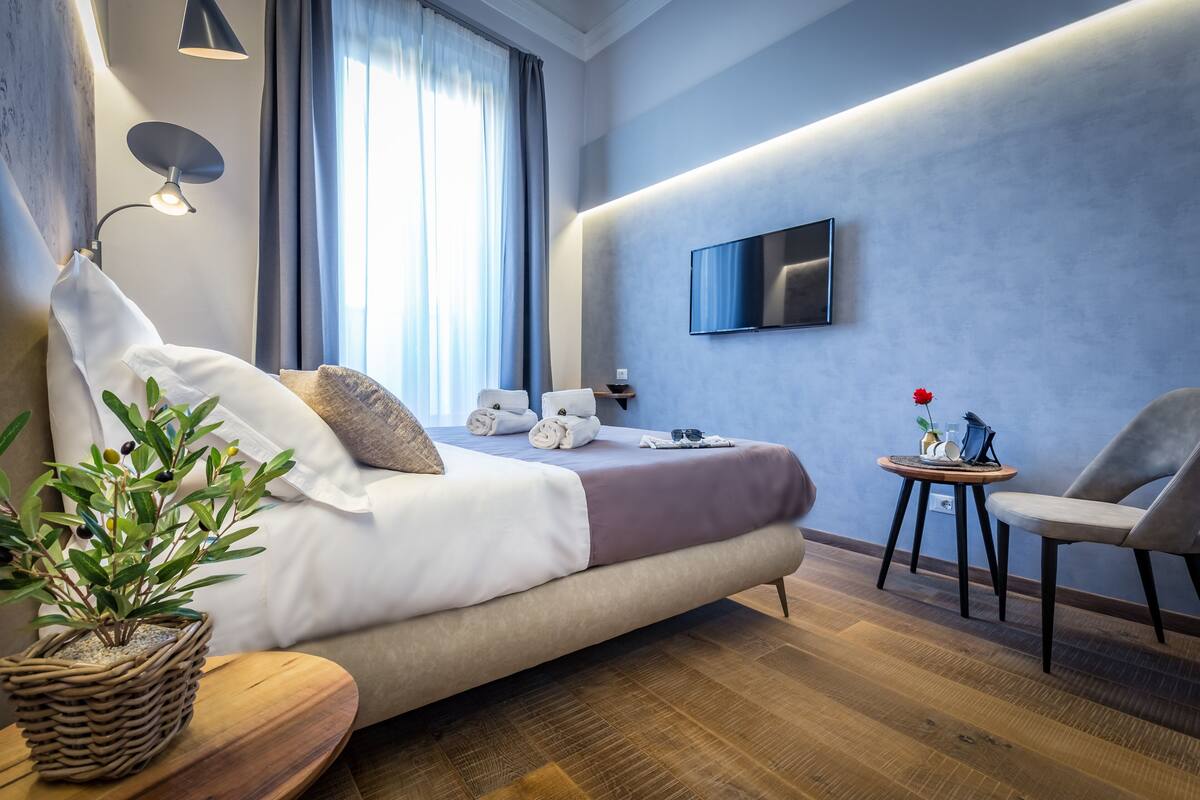 Een moderne hotelkamer met een bed, een televisie, een klein tafeltje met een vaas en een stoel.
