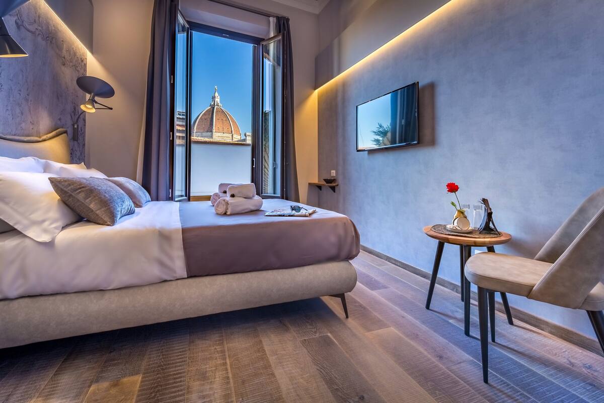 Een moderne hotelkamer met een groot bed, een klein tafeltje met een vaas en een stoel.