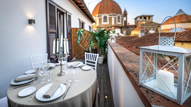 Une table dressée pour le dîner, agrémentée de bougies et d’une lanterne, sur un balcon donnant sur un bâtiment historique surmonté d’un dôme.