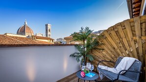 Une terrasse dotée d  ’un sol en bois, une table ronde avec une chaise, une petite plante en pot et, en arrière-plan, une vue sur un dôme et une tour.