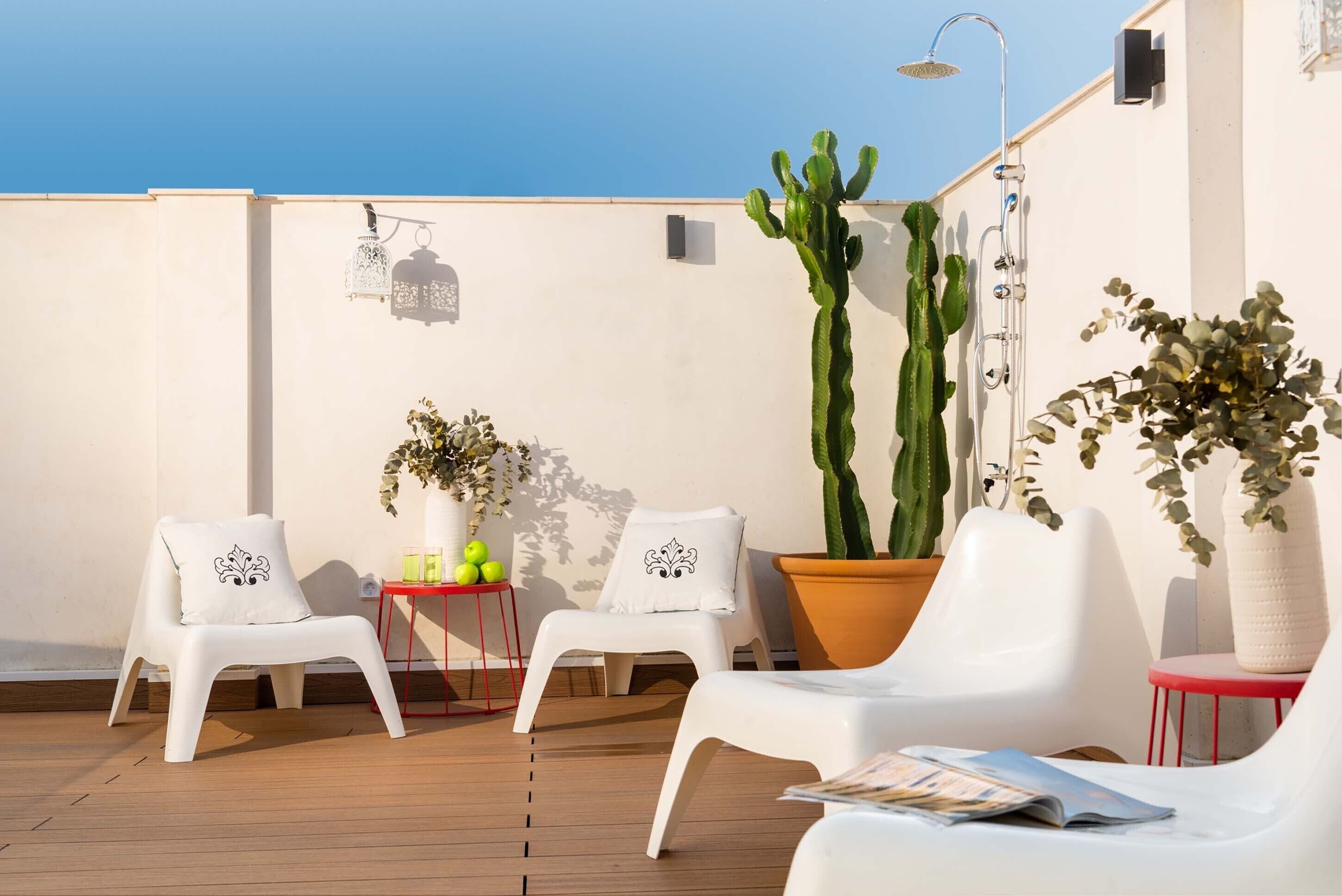 A rooftop terrace with white plastic chairs, a potted cactus, and a small table with decorative items.