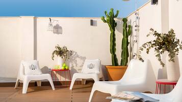 A rooftop terrace with white plastic chairs, a potted cactus, and a small table with decorative items.