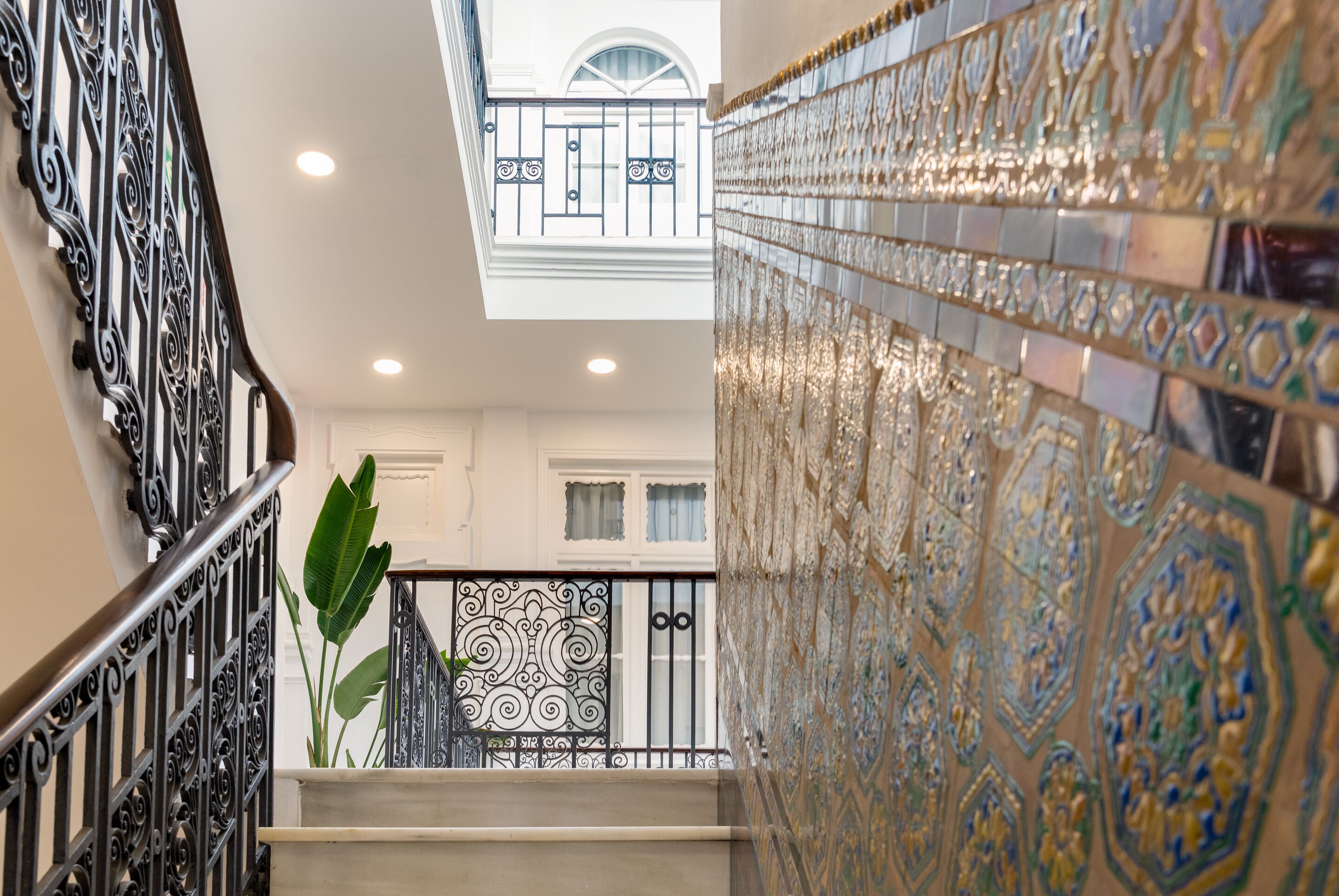 Una escalera con barandillas negras ornamentadas y vista a un balcón con azulejos decorativos.