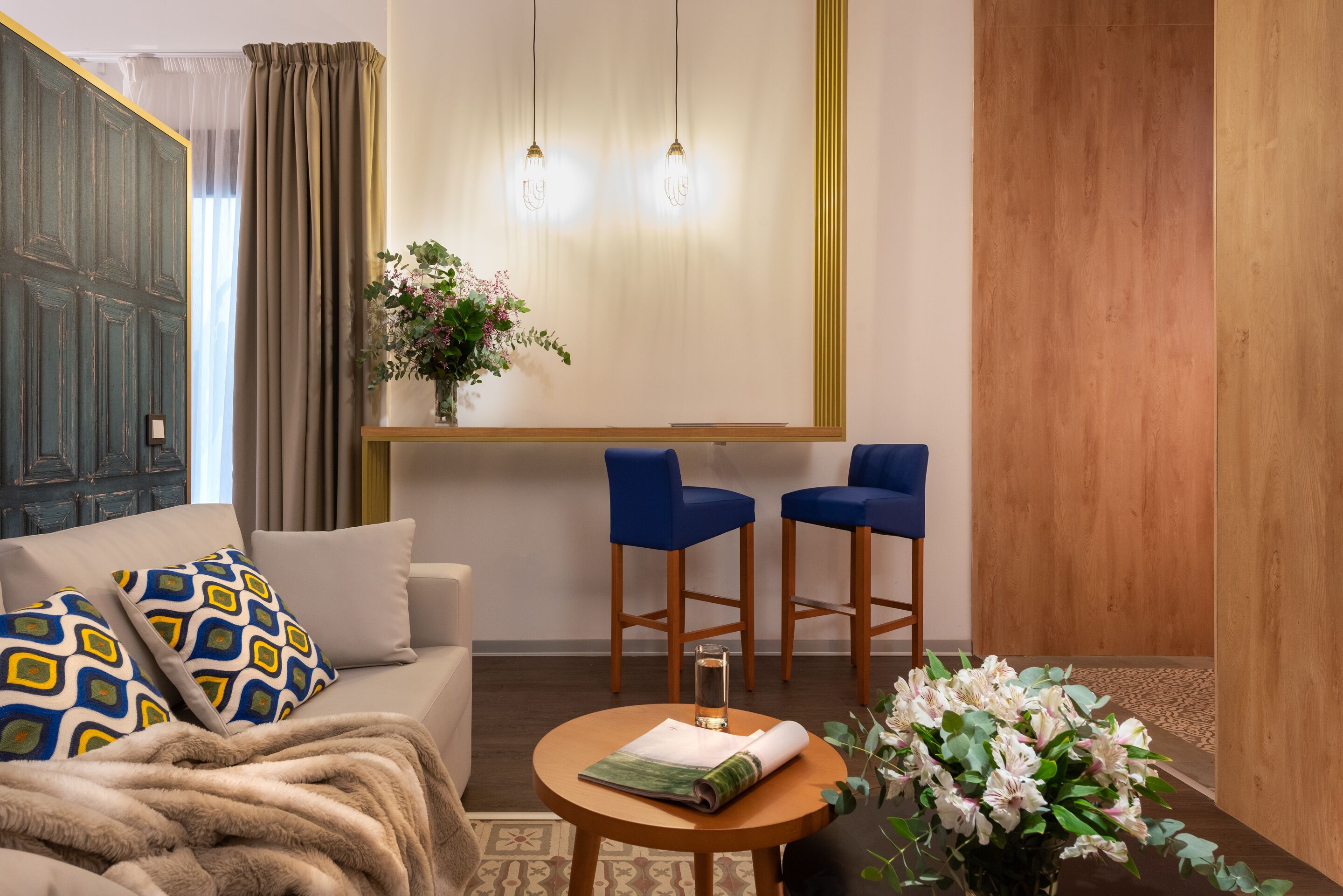 Une pièce chaleureuse avec un canapé, deux fauteuils bleus, une petite table sur laquelle est posé un vase de fleurs et un mur recouvert de panneaux de bois.