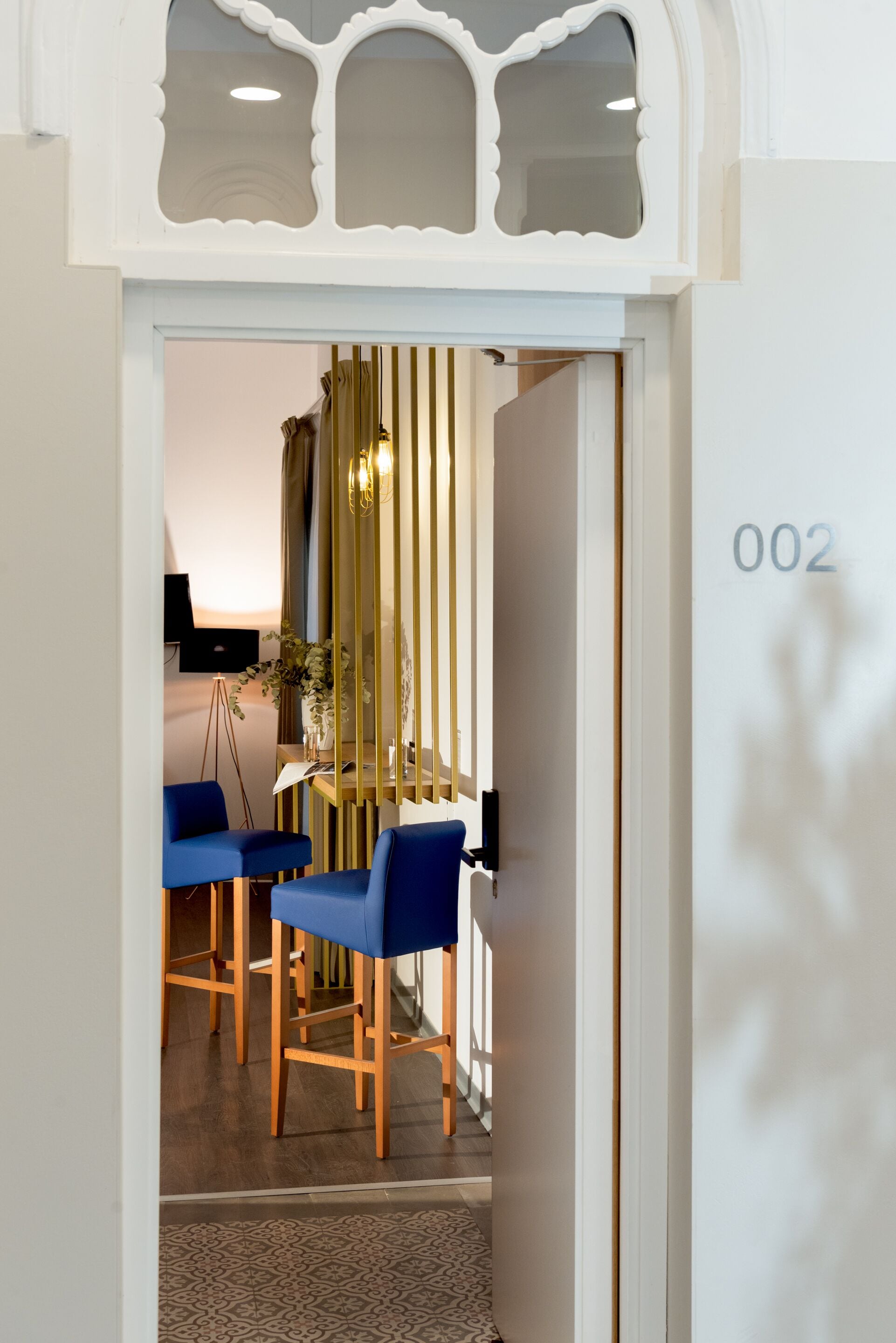 A room with a wooden floor, a desk with a chair, and a number '002' on the wall.