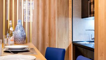 Un coin repas en bois avec une table dressée pour deux personnes, une chaise bleue et un vase posé sur la table.