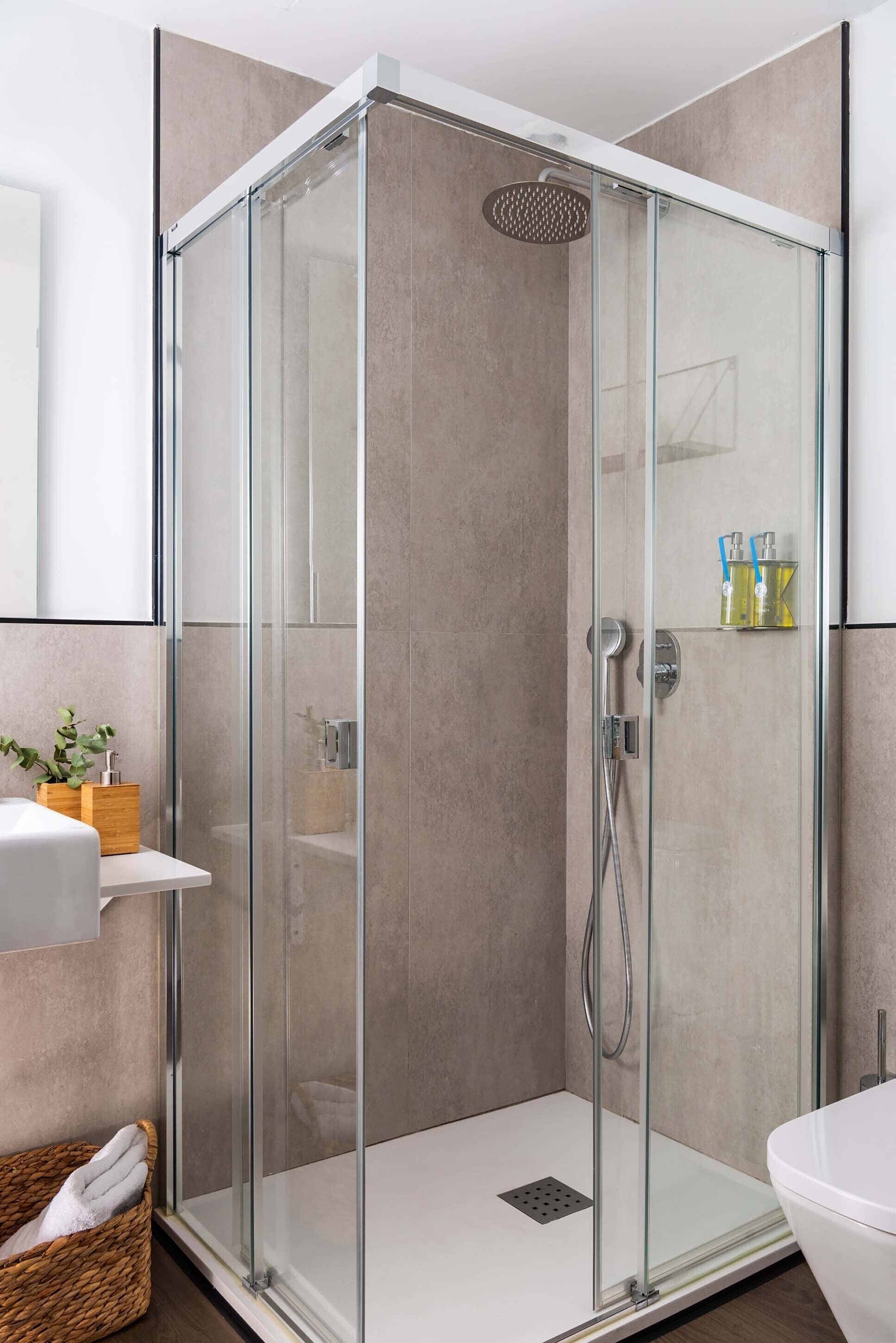 Une cabine de douche moderne avec une porte en verre, un lavabo blanc et un panier en osier.