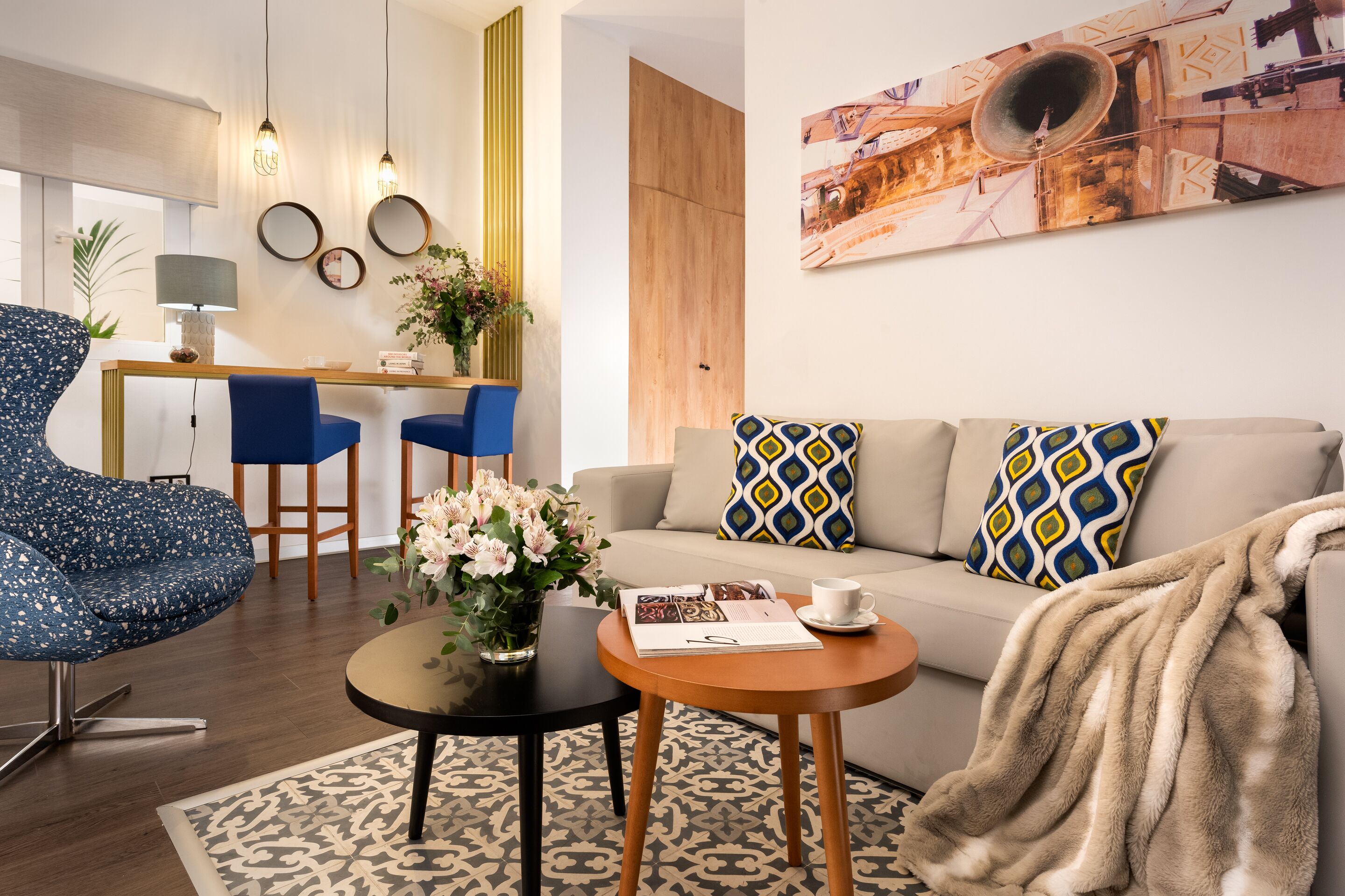 A modern living room with a sofa, a blue armchair, a coffee table, and a dining area with chairs and a lamp.