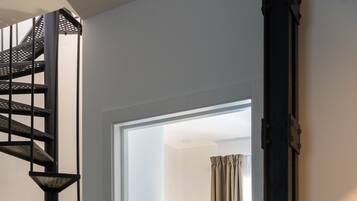 Habitación de hotel moderna con una escalera espiral, un escritorio con lámpara, una silla azul y una cama.