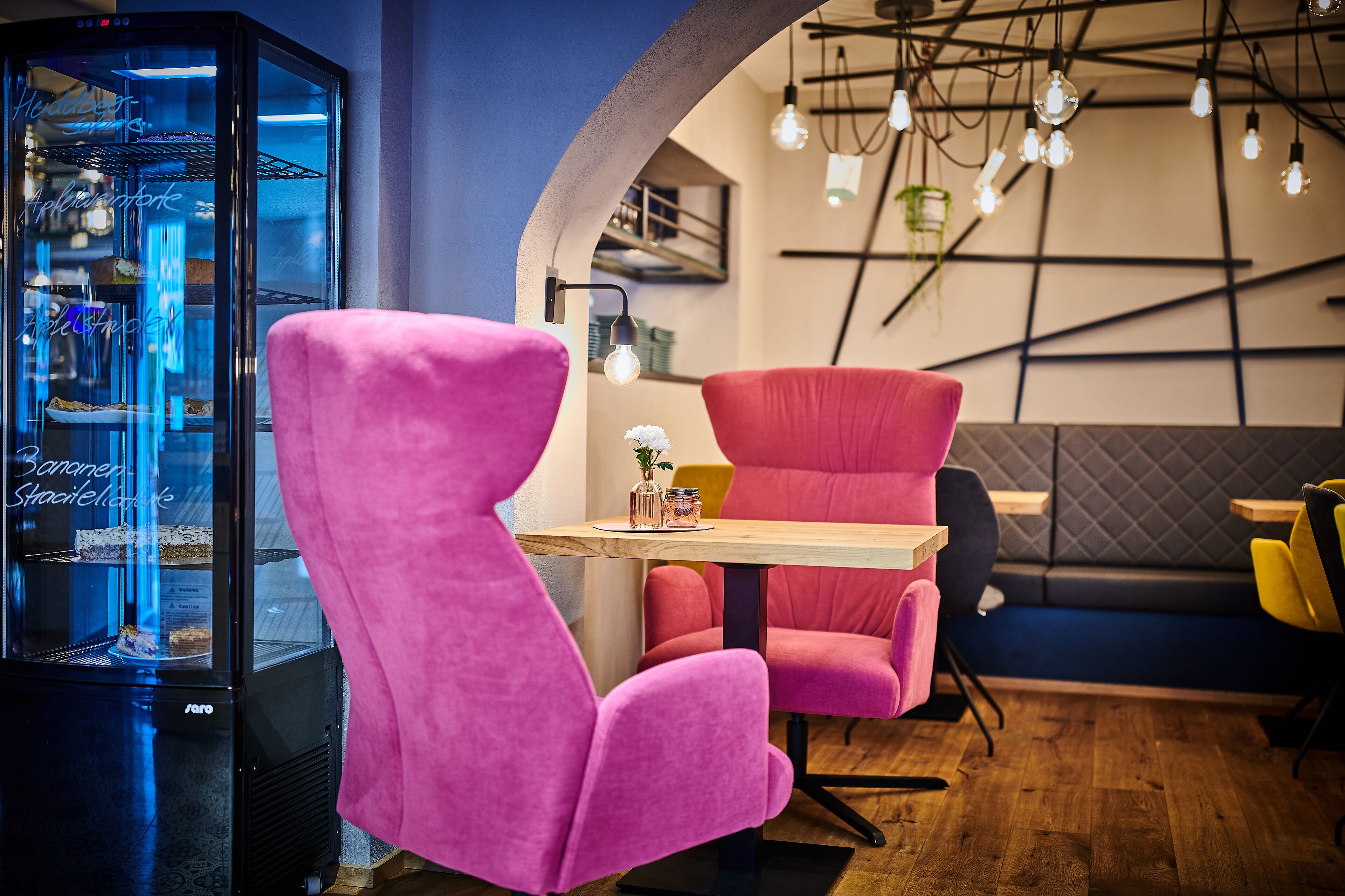 A modern interior with pink chairs, a wooden table, and a glass display case.