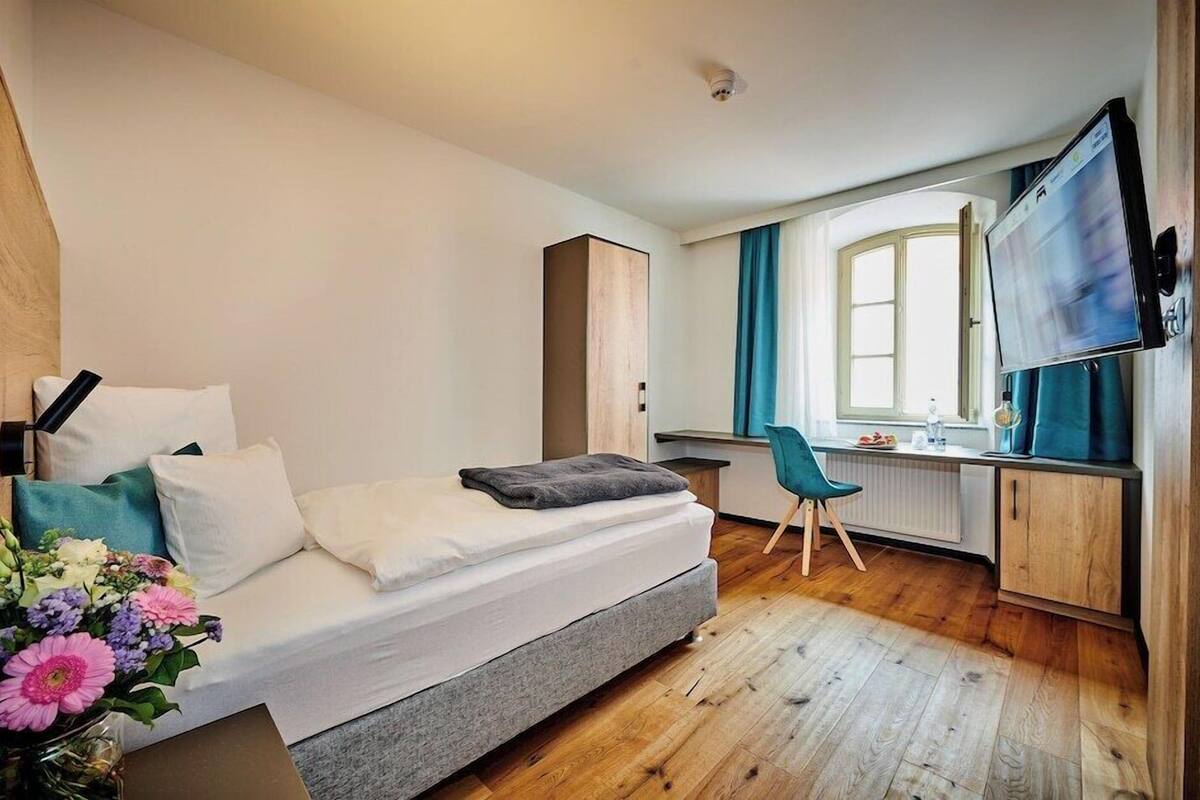 Una habitación de hotel moderna con cama, escritorio, silla, televisor y ventana.