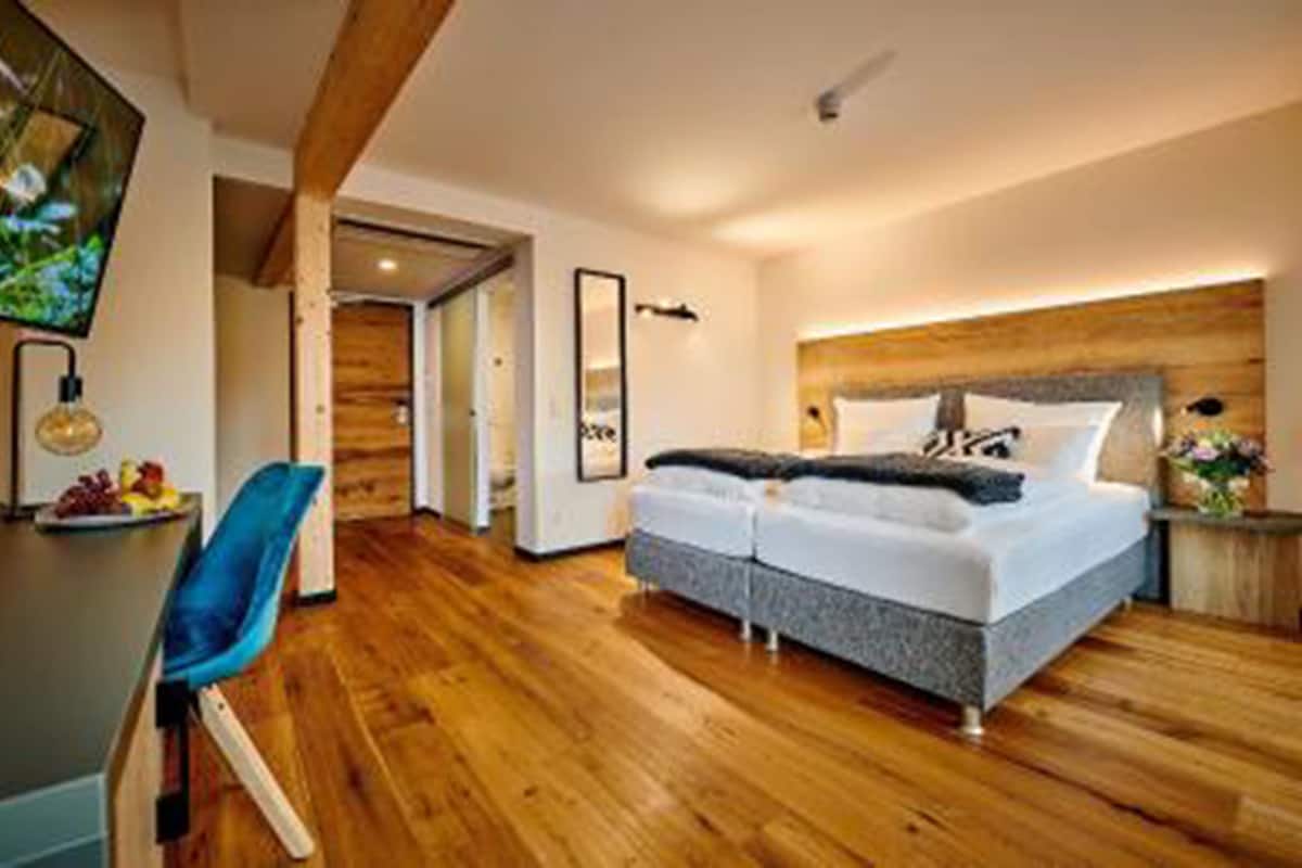 Un dormitorio moderno con una cama grande, piso de madera, un escritorio con silla y un televisor en la pared.