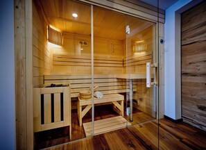 Eine Sauna mit Holzbänken und einer Glastür, eine Holzbank mit Handtuch und Eimer, sowie eine Holzwand mit Holztür.