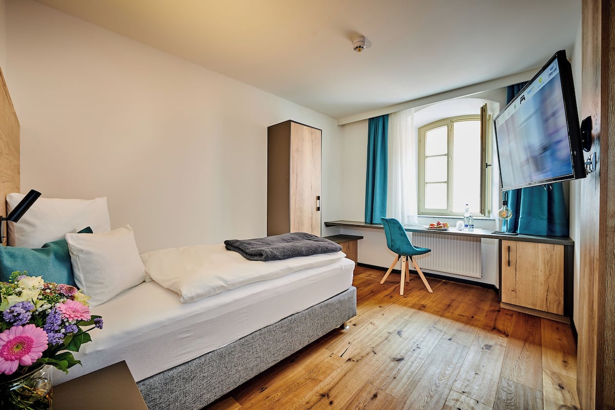 Un dormitorio con cama, escritorio, silla, televisor y ventana.