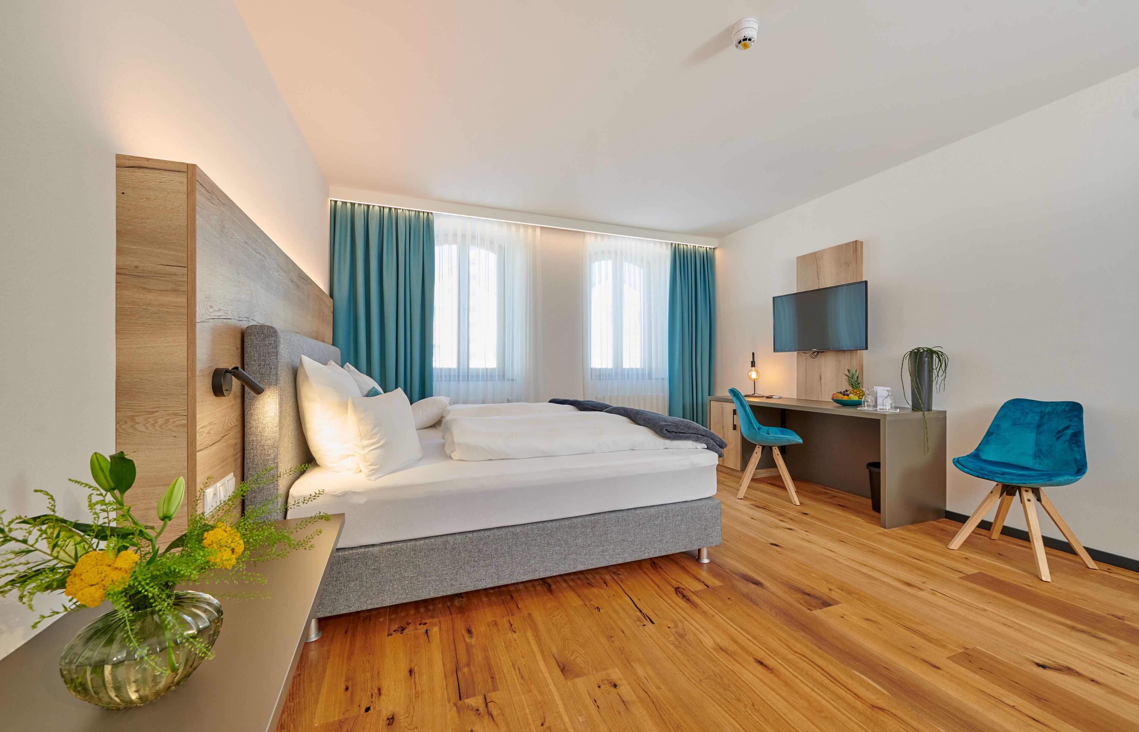 A modern hotel room with a bed, a desk, a chair, and a TV.