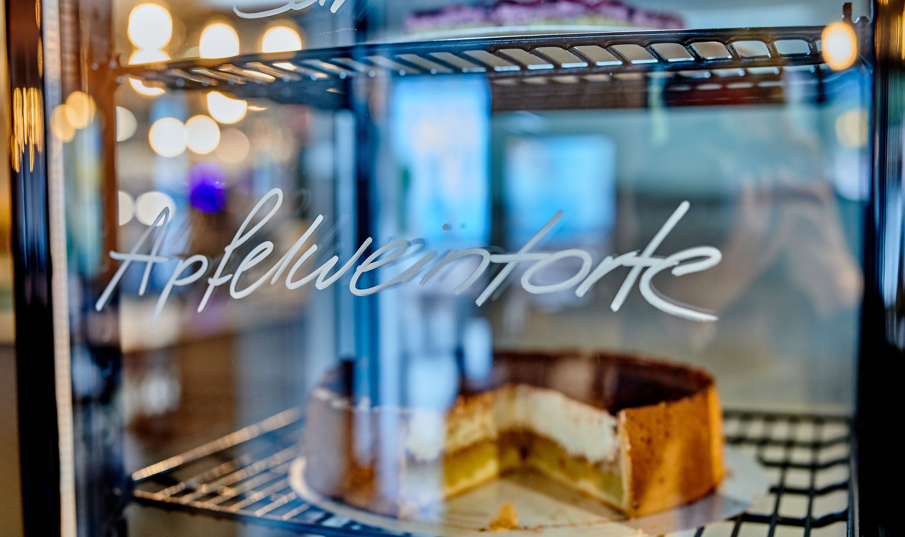 A dessert display case with a cake and a glass of beverage.