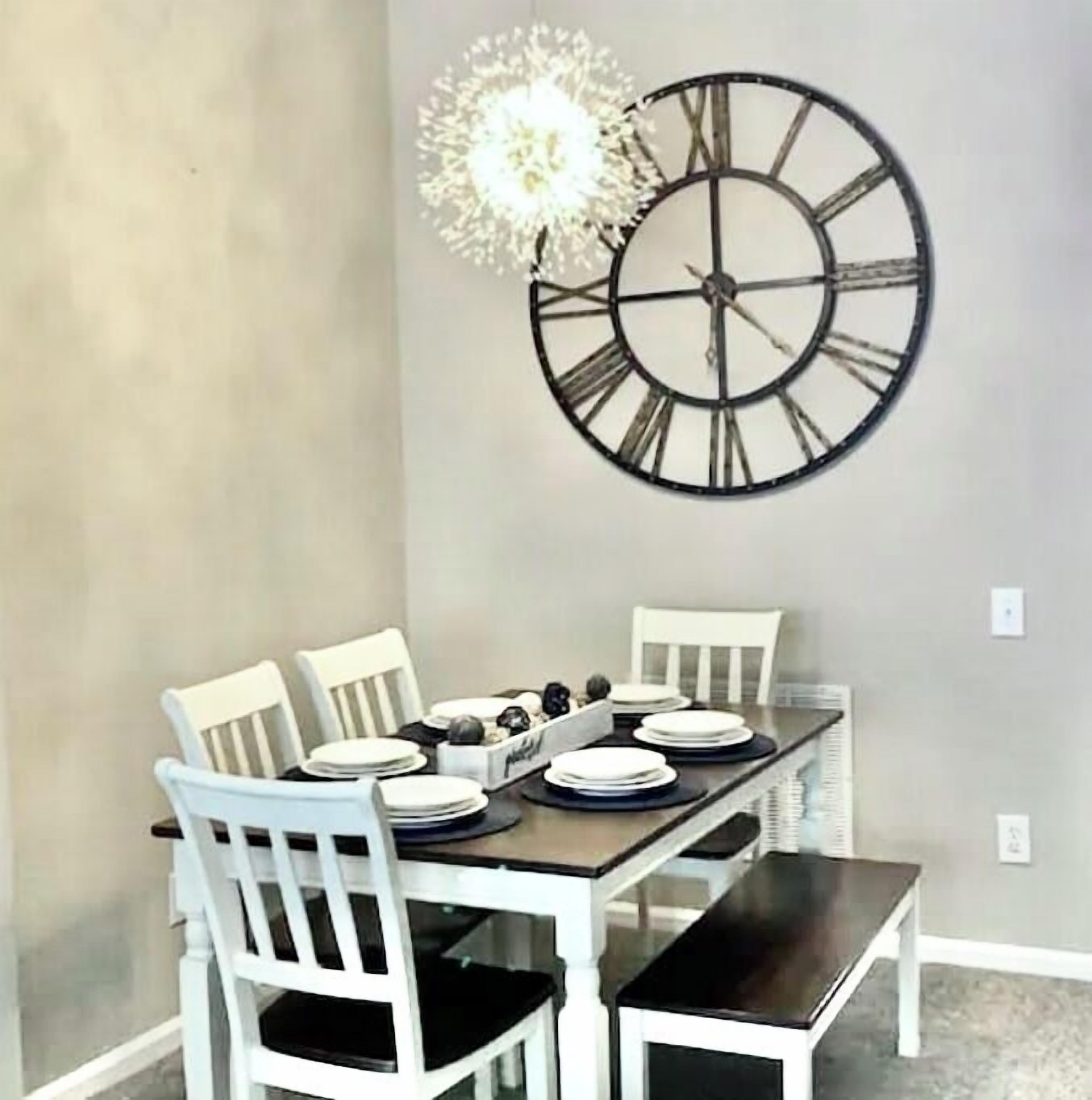 Un coin repas avec une table dressée pour quatre personnes, des chaises blanches et une grande horloge murale.