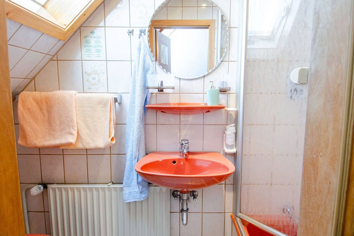 Une salle de bain avec un puits de lumière, un lavabo rouge, un miroir et deux serviettes.