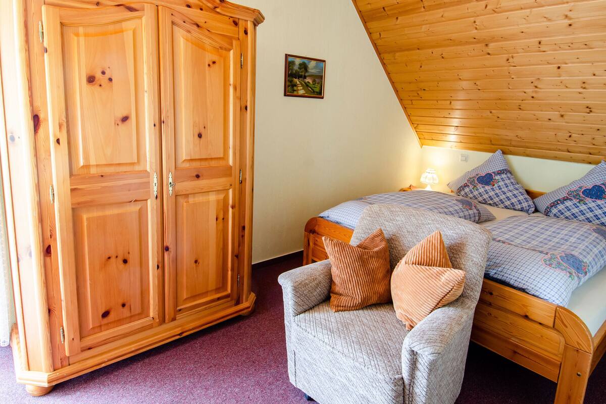 Une chambre avec une armoire en bois, un lit recouvert d’une couette à carreaux et un petit tableau accroché au mur.