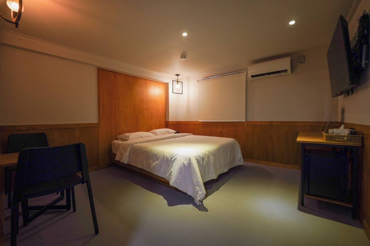 Una habitación de hotel con una cama, un escritorio, una silla, un televisor y un equipo de aire acondicionado.