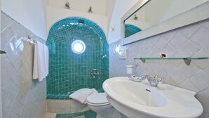 A bathroom with a white sink, a toilet, and a shower with green tiles. - Suite Malu' (Praiano)