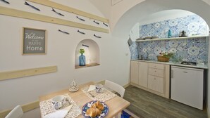 A dining area with a table set for two, a kitchen with blue and white patterned tiles, and a welcome sign on the wall. - Suite Malu' (Praiano)