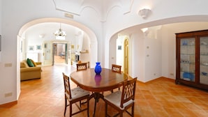 A dining area with a round wooden table, four chairs, and a blue vase. There is a sofa and a cabinet in the background. - Casa Alessia (Praiano)