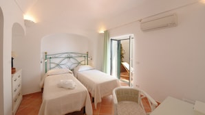 A bedroom with two single beds, a chair, a desk, and an air conditioning unit. - Casa Alessia (Praiano)