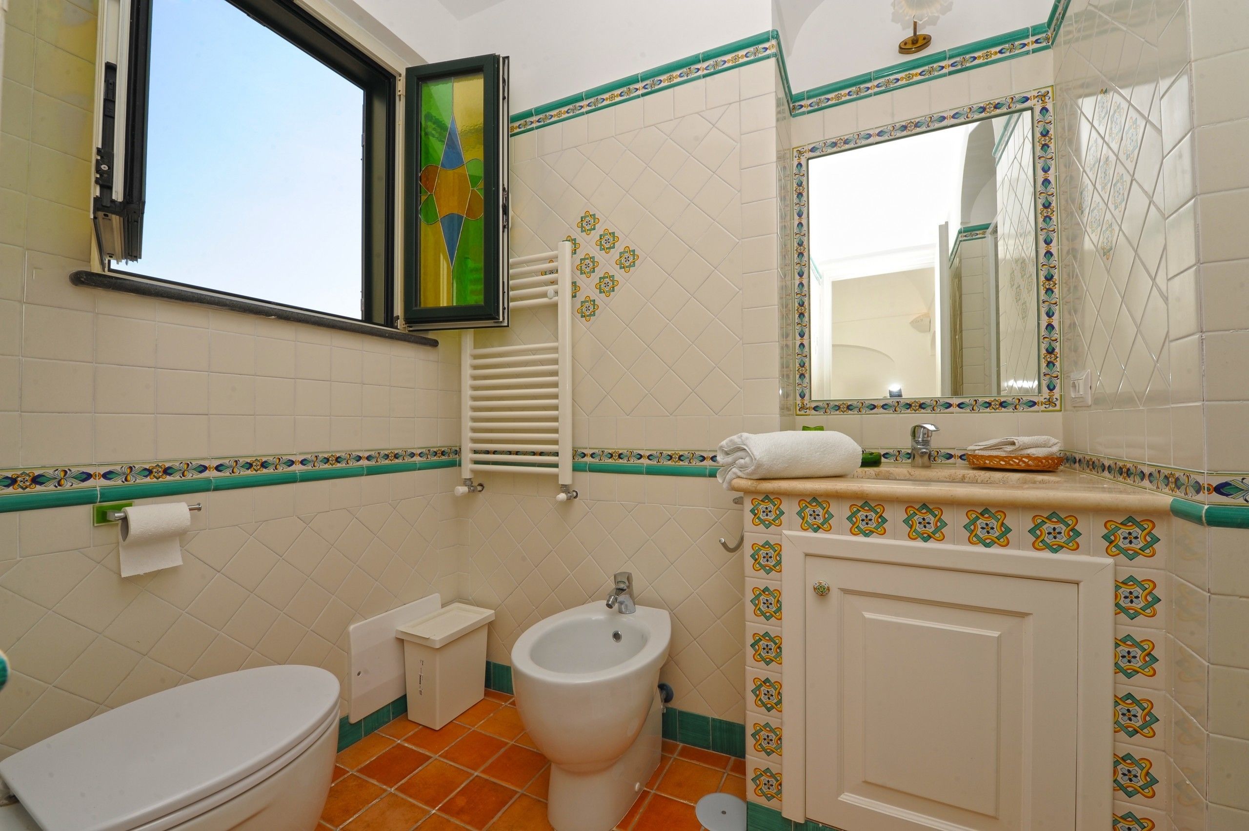 Een badkamer met toilet, bidet, wastafel, spiegel en decoratieve tegels.