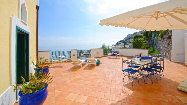 A terrace with outdoor seating, a view of the sea, and a stone wall. - Casa Giorgia (Praiano)