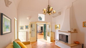A spacious living room with a sofa, a fireplace, and a view of the outside. - Casa Giorgia (Praiano)
