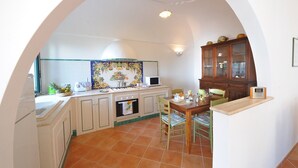 A kitchen with a tiled backsplash, a stove, a microwave, and a dining area with chairs and a table. - Casa Giorgia (Praiano)
