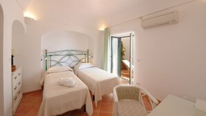 A bedroom with two beds, a chair, a dresser, and a sliding glass door leading to an outdoor area. - Casa Giorgia (Praiano)