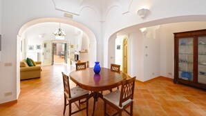 A spacious dining area with a round wooden table and chairs, a blue vase centerpiece, and a traditional cabinet with glass doors. - Casa Giorgia (Praiano)