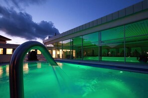 Ein modernes Gebäude mit großen Glasfenstern, die den Himmel und den Poolbereich mit grüner Beleuchtung reflektieren.