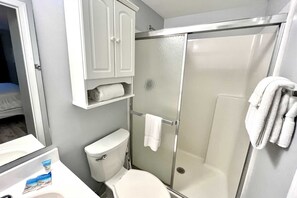 A bathroom with a toilet, a shower enclosure, and a cabinet above the toilet. - Royal Palms 402 1 Bedroom Condo by RedAwning (Gulf Shores)