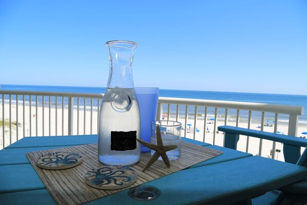 A table with a bottle, a glass, and a starfish on a blue tablecloth, overlooking a beach. - Royal Palms 402 1 Bedroom Condo by RedAwning (Gulf Shores)