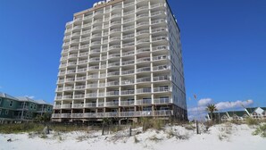 A tall, multi-story hotel with balconies, located near a beach with sand and sparse vegetation. - Royal Palms 402 1 Bedroom Condo by RedAwning (Gulf Shores)
