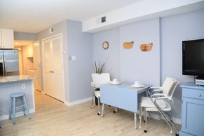 A modern kitchen with a built-in refrigerator, a dining area with a table and chairs, and a television on a stand. - Royal Palms 402 1 Bedroom Condo by RedAwning (Gulf Shores)