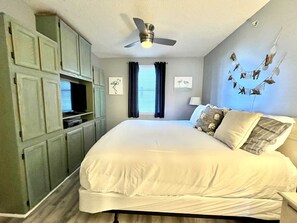 A bedroom with a large bed, a ceiling fan, and a TV on a cabinet.
