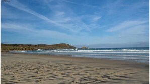 A beach with sand, waves, and a clear sky. - Spa Suites Odeon (Naron)