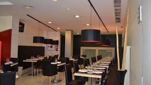 A modern restaurant with long tables, black chairs, and red pendant lights. - Spa Suites Odeon (Naron)