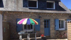 Una casa de piedra con terraza de madera, una mesa con sillas, un paraguas colorido y una bicicleta.