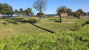Un parque con juegos infantiles, una estructura de madera y un cuerpo de agua al fondo.