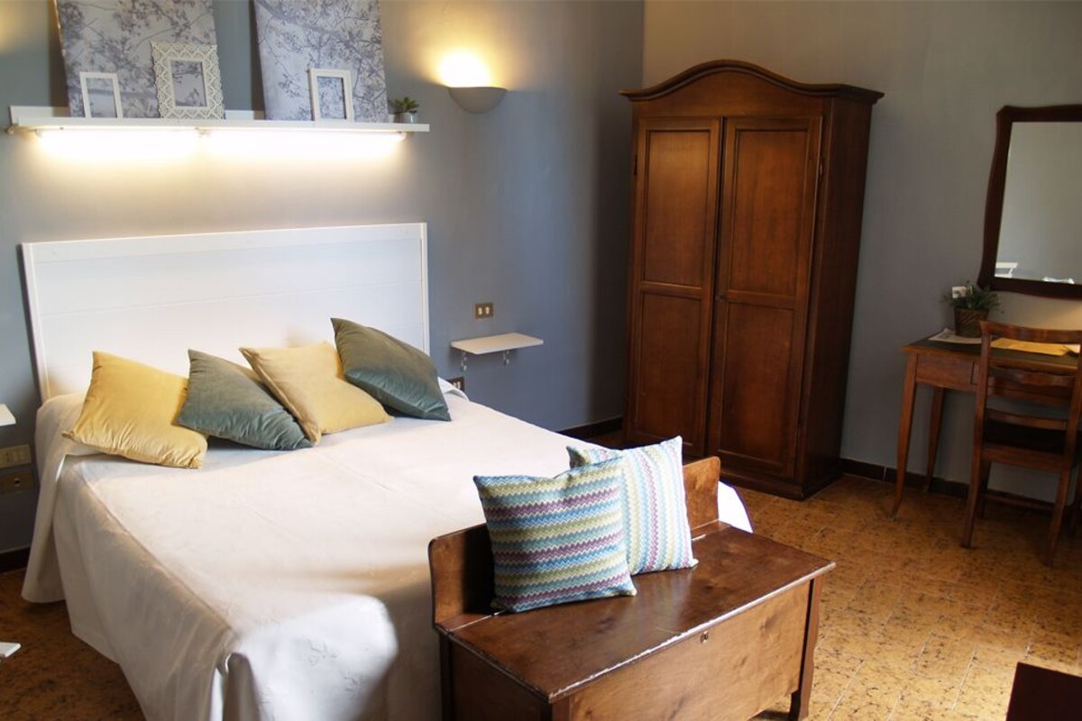 A bedroom with a bed, bedside tables, a wooden wardrobe, and a desk with a chair.