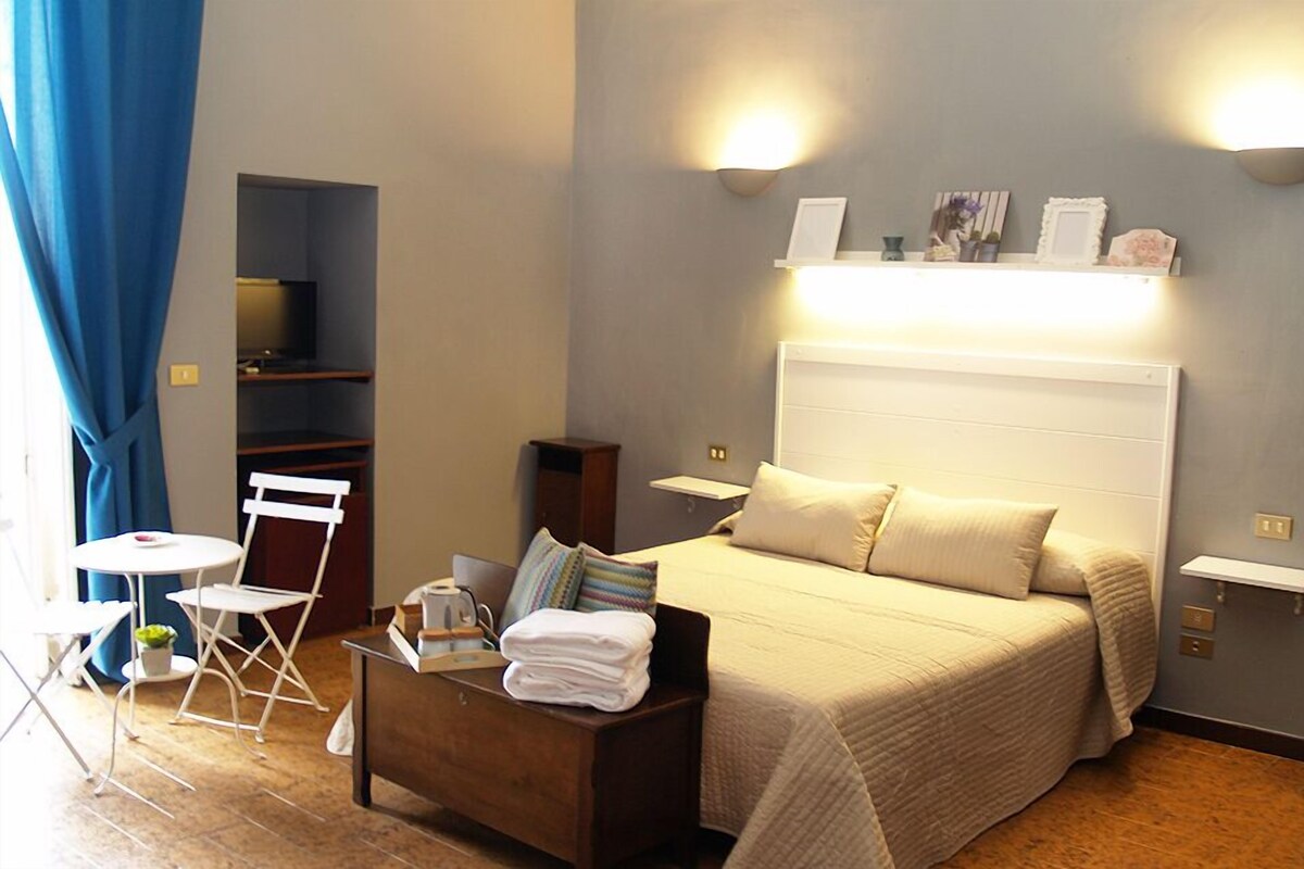 A hotel room with a bed, bedside tables, a desk, a chair, a small table, and a TV.