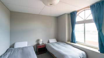 A bedroom with two single beds, a nightstand with a lamp, a window with curtains, and a ceiling fan.