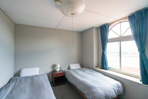 A bedroom with two single beds, a nightstand with a lamp, a window with curtains, and a ceiling fan. - Guesthouse leaf (Hokuto)