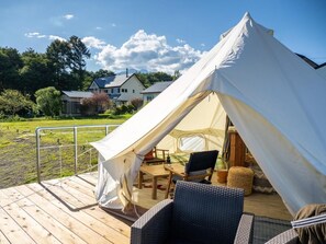A large tent with a wooden deck, a table, and chairs, set against a backdrop of houses and trees. - Guesthouse leaf (Hokuto)